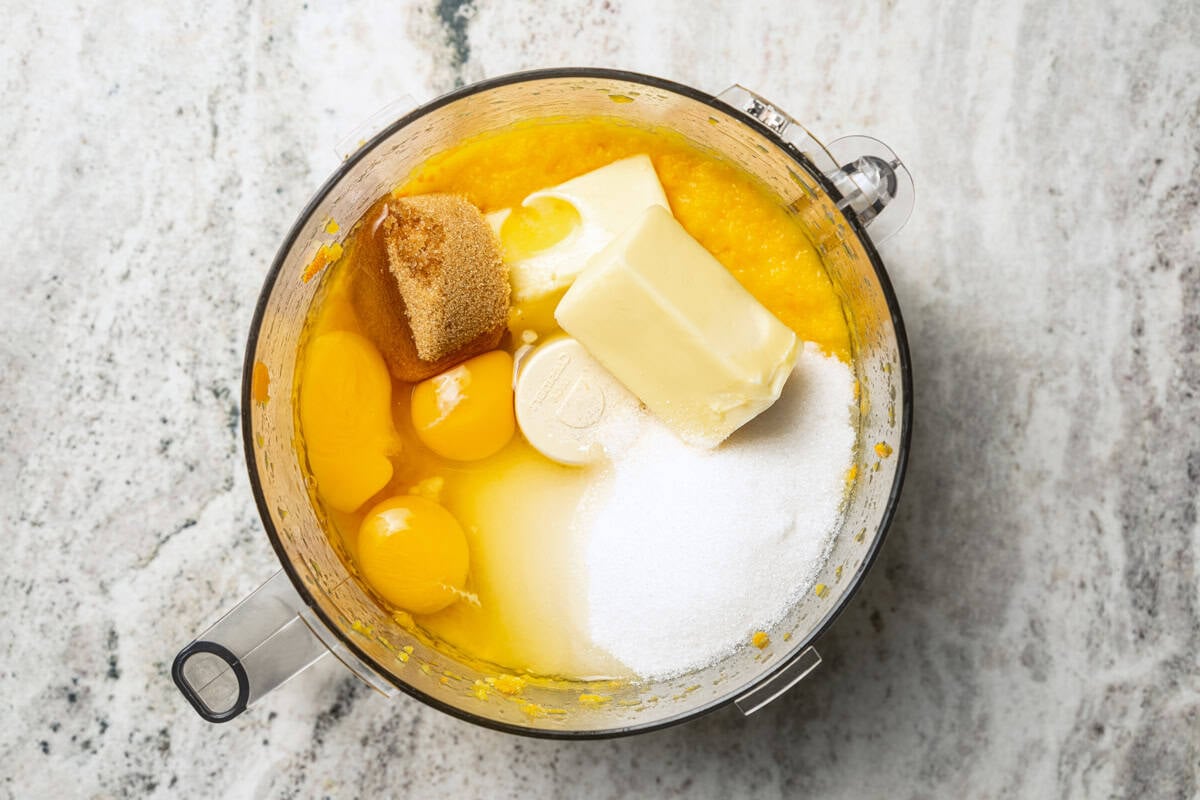 This orange cake recipe uses whole oranges, peels and all! It's moist and full of sweet citrus flavor, drenched in orange glaze. Orange cake batter ingredients added to a food processor.