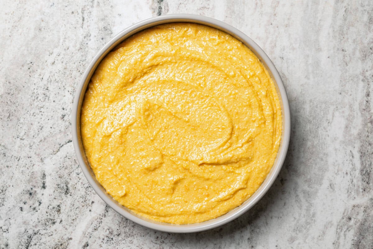 This orange cake recipe uses whole oranges, peels and all! It's moist and full of sweet citrus flavor, drenched in orange glaze. Cake batter in a round pan.