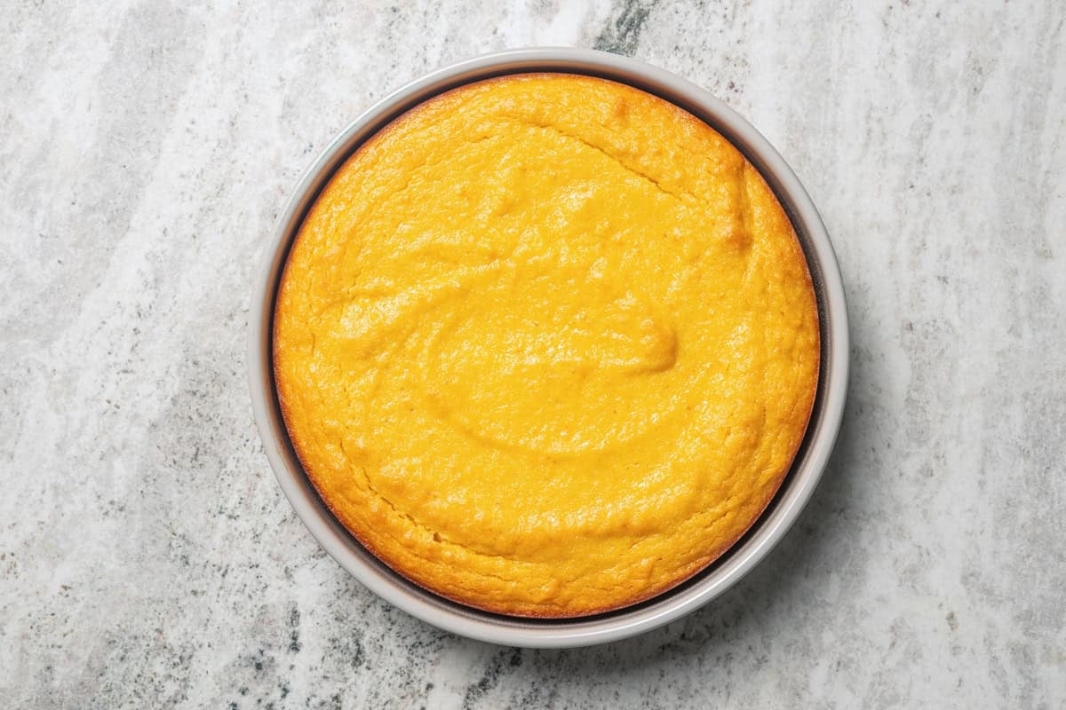 This orange cake recipe uses whole oranges, peels and all! It's moist and full of sweet citrus flavor, drenched in orange glaze. Baked orange cake in a round pan.