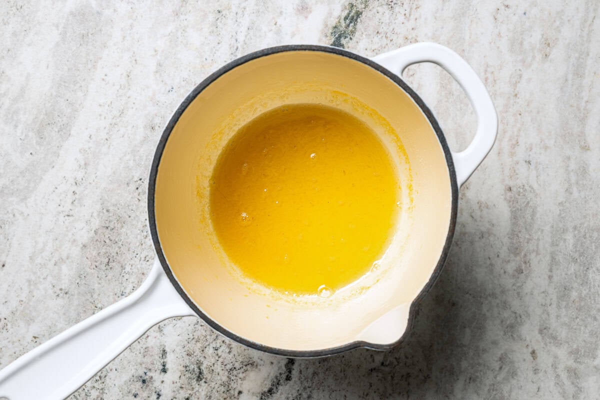 This orange cake recipe uses whole oranges, peels and all! It's moist and full of sweet citrus flavor, drenched in orange glaze. Orange glaze in a saucepan.