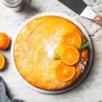 An orange cake dusted with powdered sugar and topped with fresh orange slices.