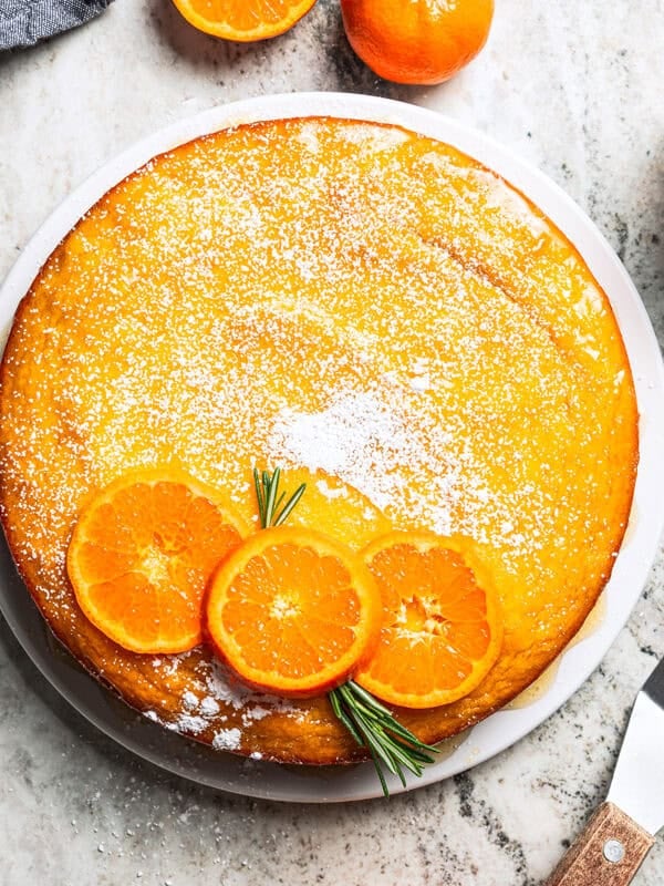 An orange cake dusted with powdered sugar and topped with fresh orange slices.