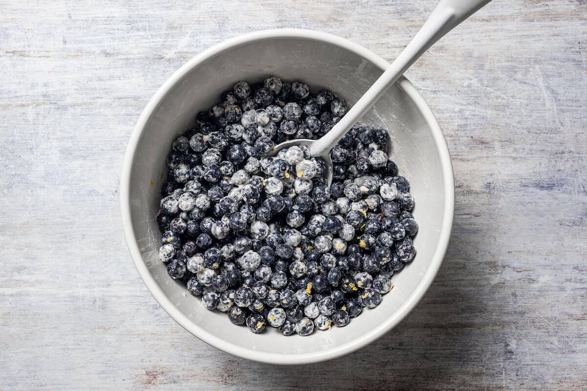 Blueberries tossed with flour and lemon zest in a bowl.