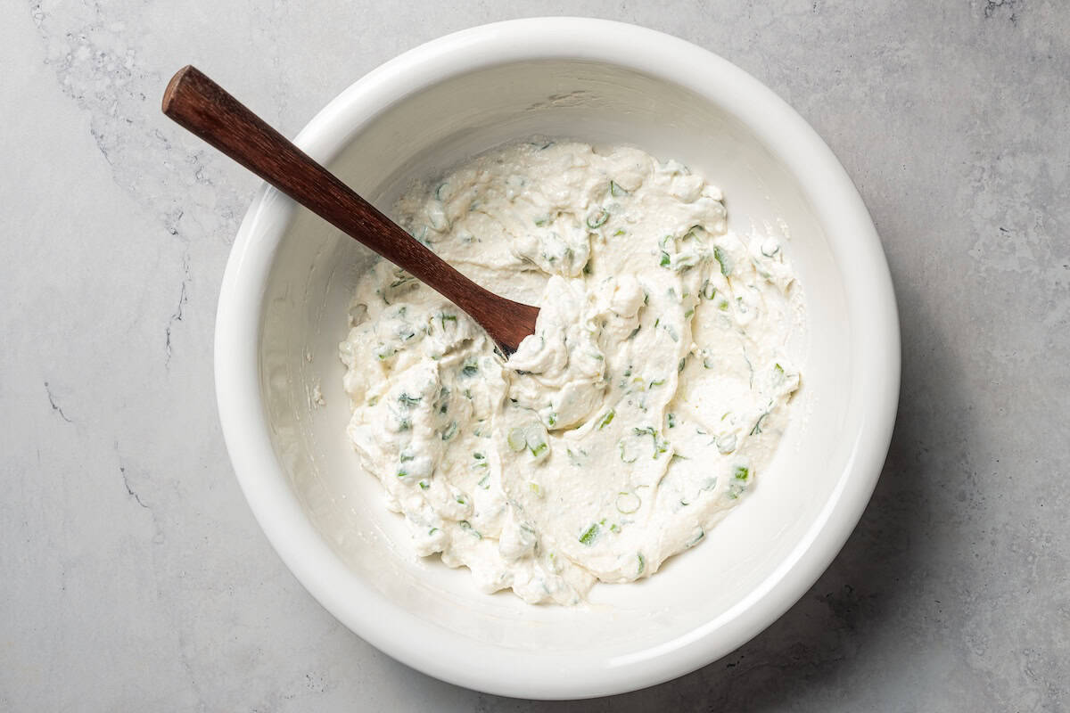 Cottage cheese combined with fresh herbs in a bowl.