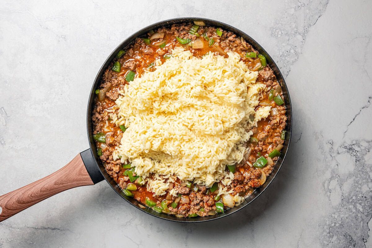 Rice added to ground meat and veggies in a skillet.