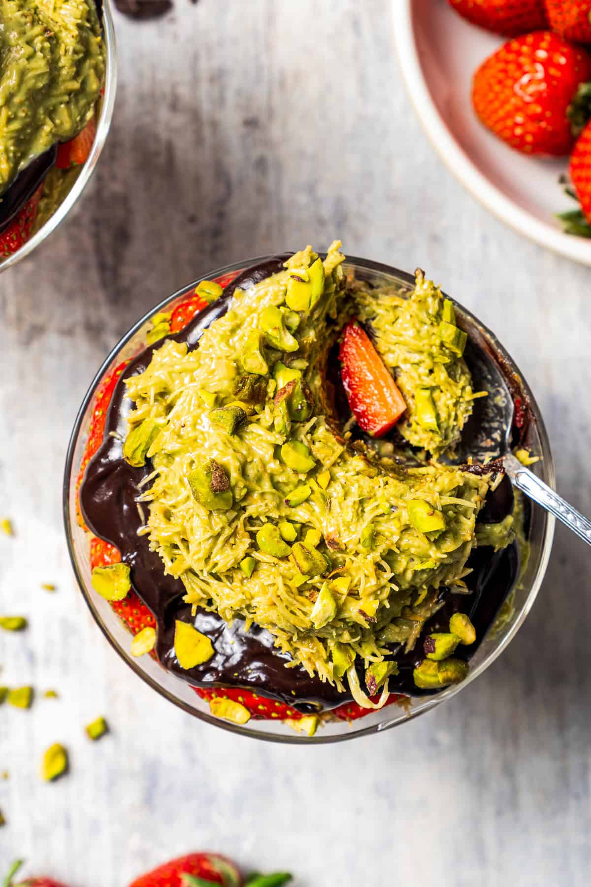 A spoon scooping out the Dubai chocolate mixture with strawberries from a glass cup.