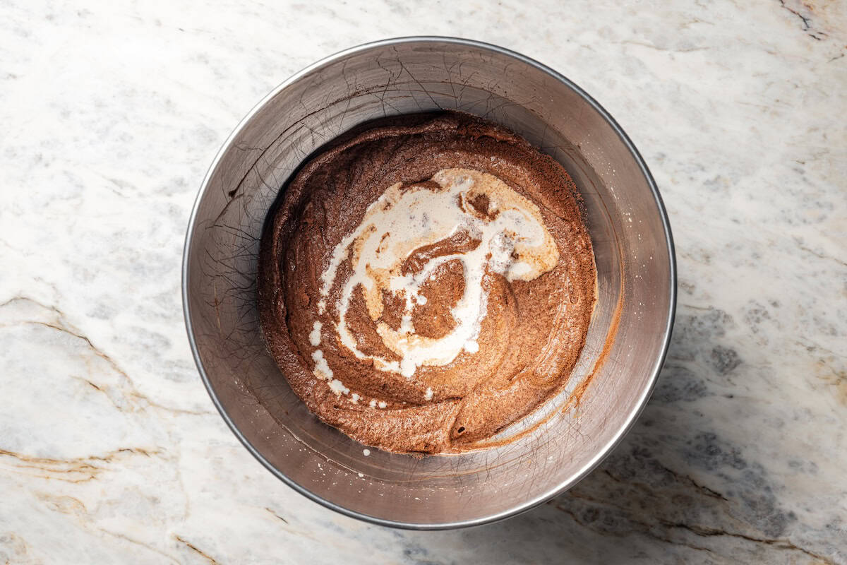 Heavy cream added to chocolate fudge cake batter in a bowl.