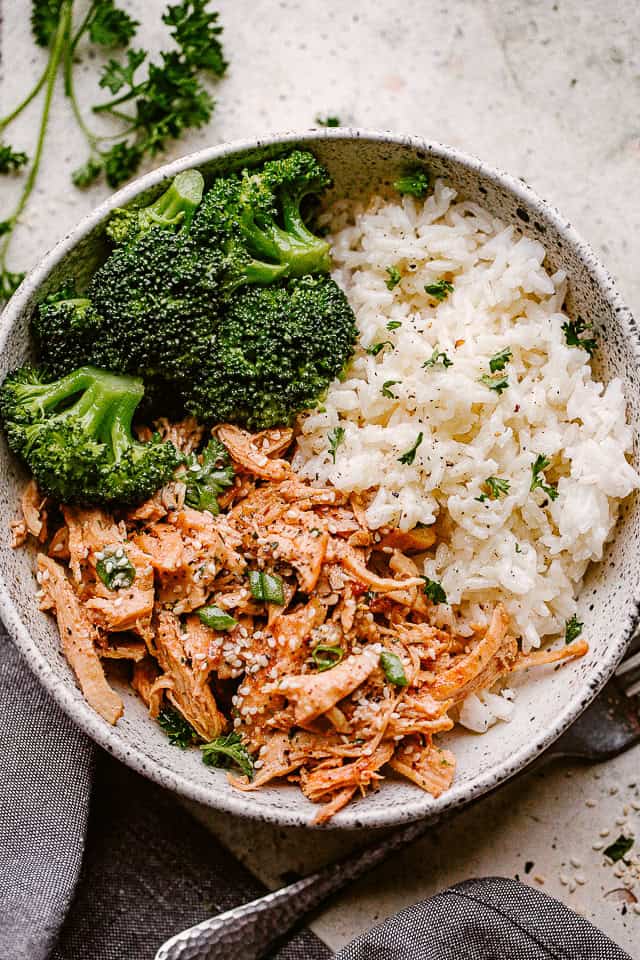 A bowl of honey garlic chicken, shredded, and served with broccoli and rice.