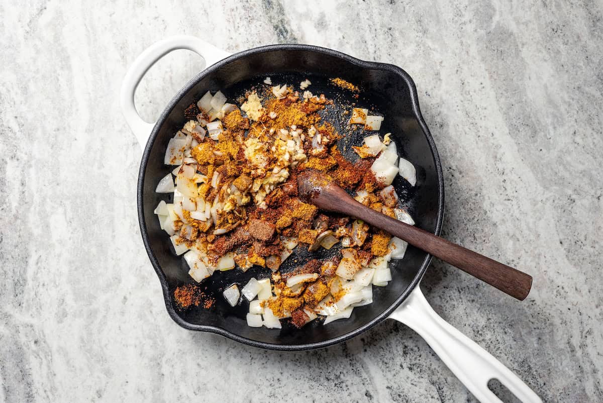Garlic, ginger, and spices added to onions in a skillet.