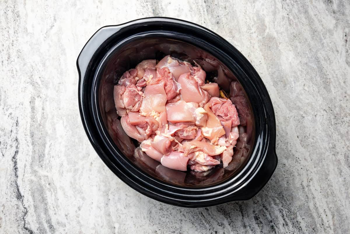 Chicken pieces added to the slow cooker on top of the onion mixture.