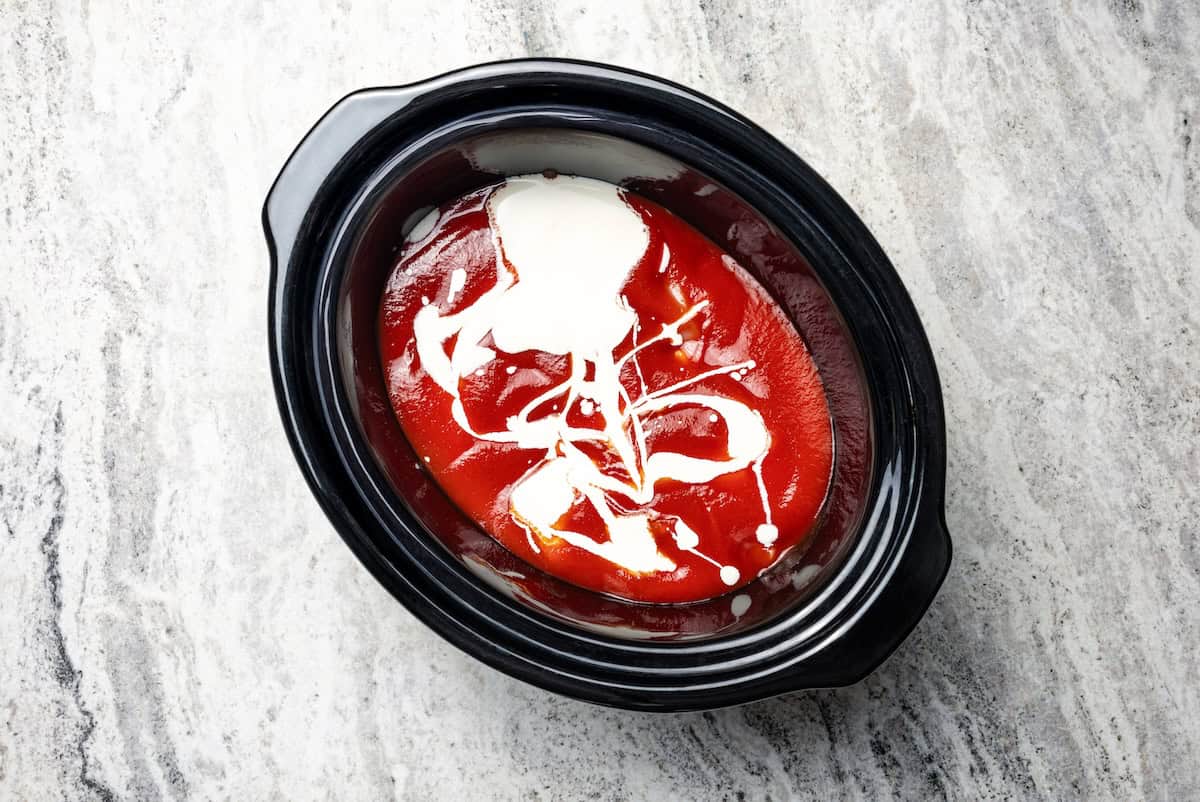 Tomato sauce and heavy cream added on top of the chicken and onions in the slow cooker.