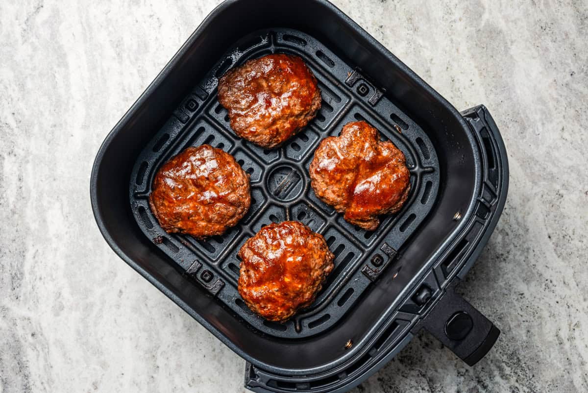 Four hamburger patties in an air fryer basket.