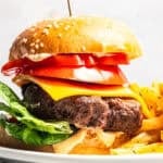 An air fryer hamburger next to fries on a plate.