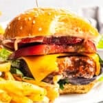 An air fryer hamburger with a bite missing next to fries on a plate.