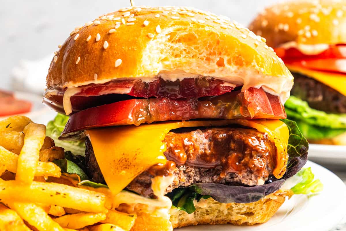 An air fryer hamburger with a bite missing next to fries on a plate.