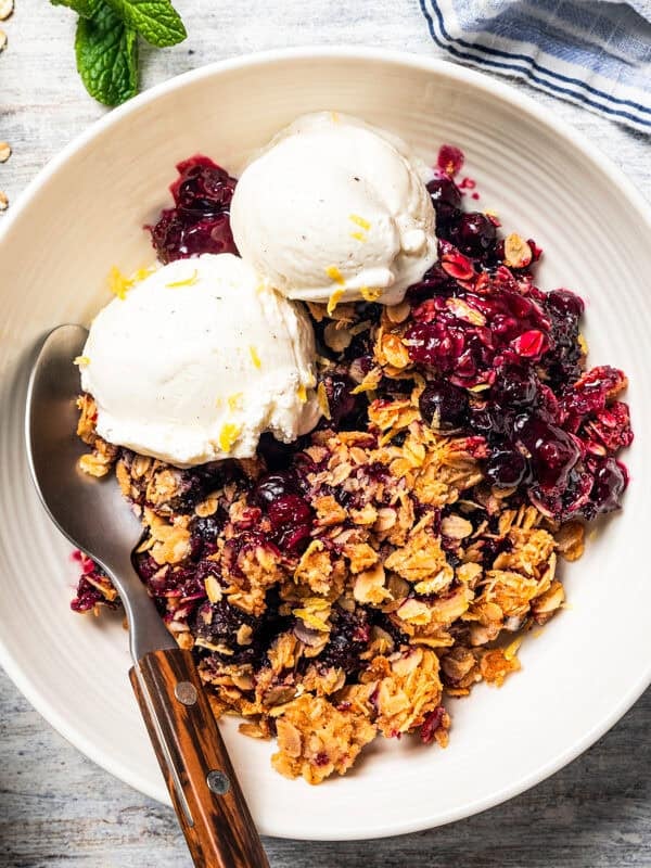A bowl of blueberry crisp topped with vanilla ice cream.