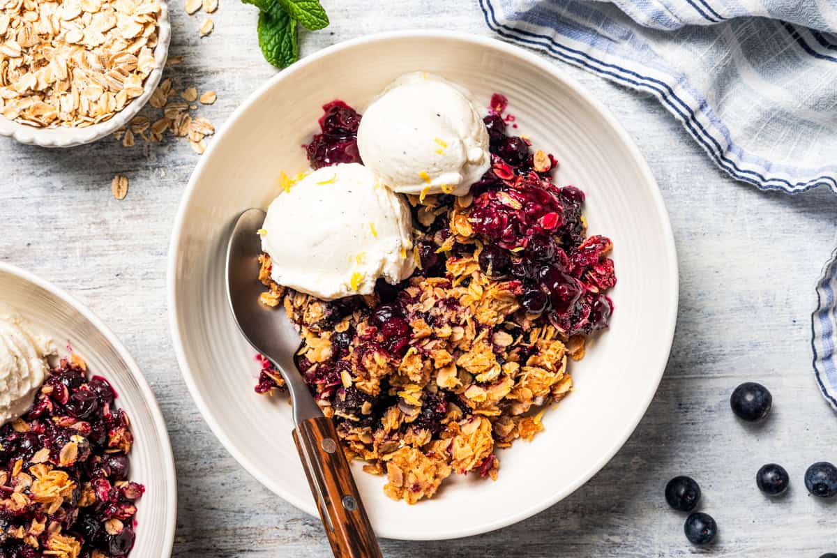 A bowl of blueberry crisp topped with vanilla ice cream.