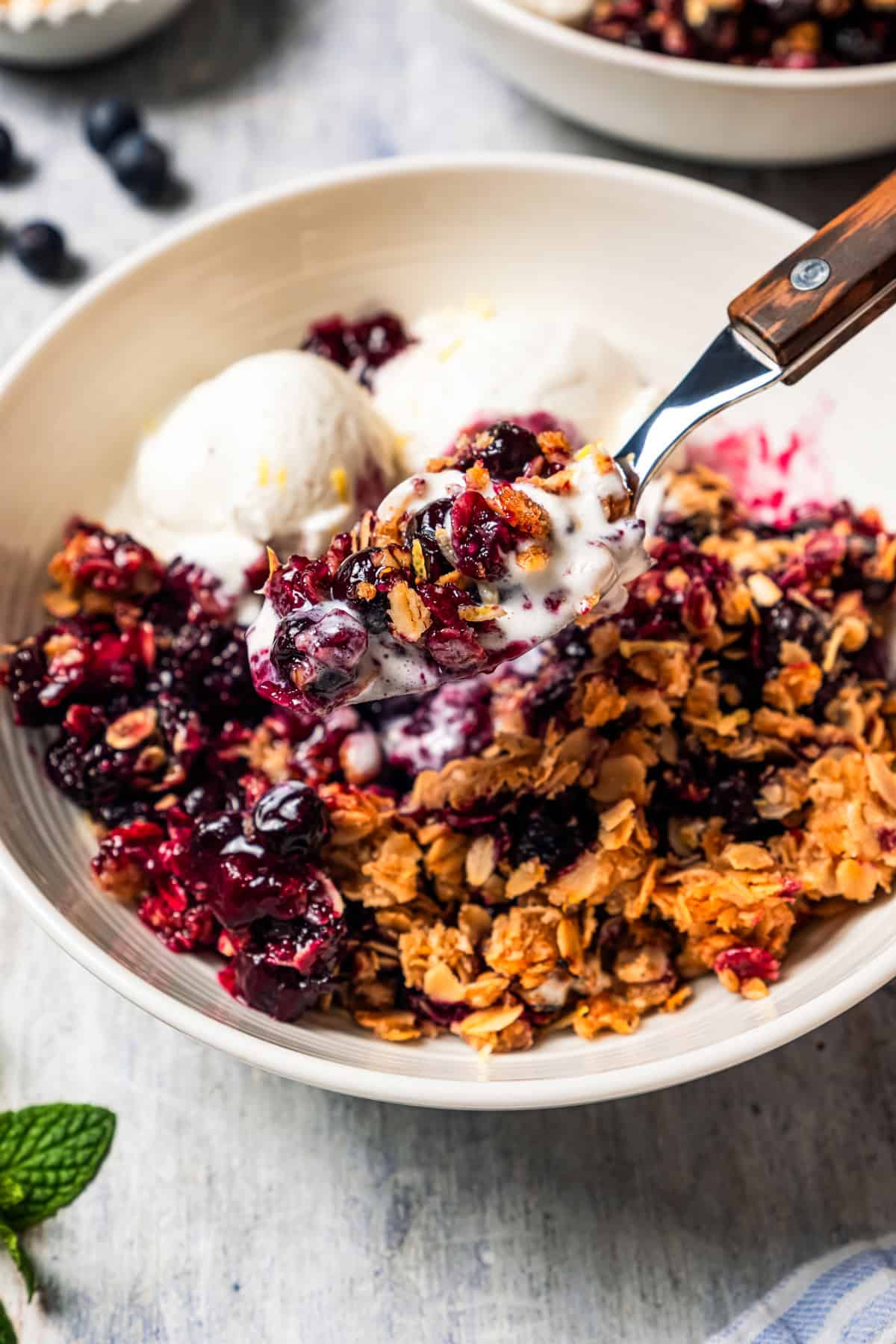 Scooping out blueberry crisp from a bowl with a spoon.