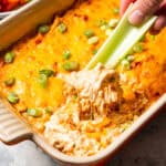 A hand dipping a celery stick into cottage cheese Buffalo chicken dip.