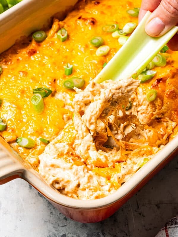 A hand dipping a celery stick into cottage cheese Buffalo chicken dip.