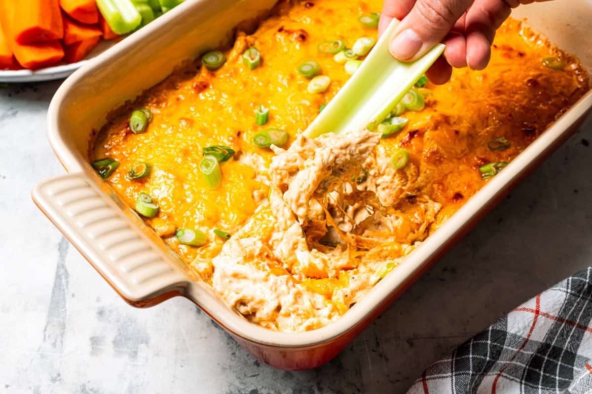 Baked cottage cheese Buffalo chicken dip is high in protein, made with three types of melty cheese. It’s rich and creamy without mayonnaise! A hand dipping a celery stick into cottage cheese Buffalo chicken dip.