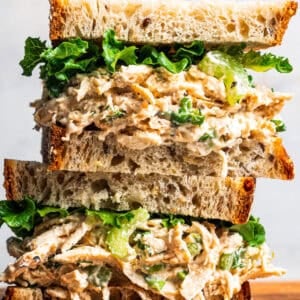 Two cottage cheese chicken salad sandwiches stacked on a wooden cutting board.
