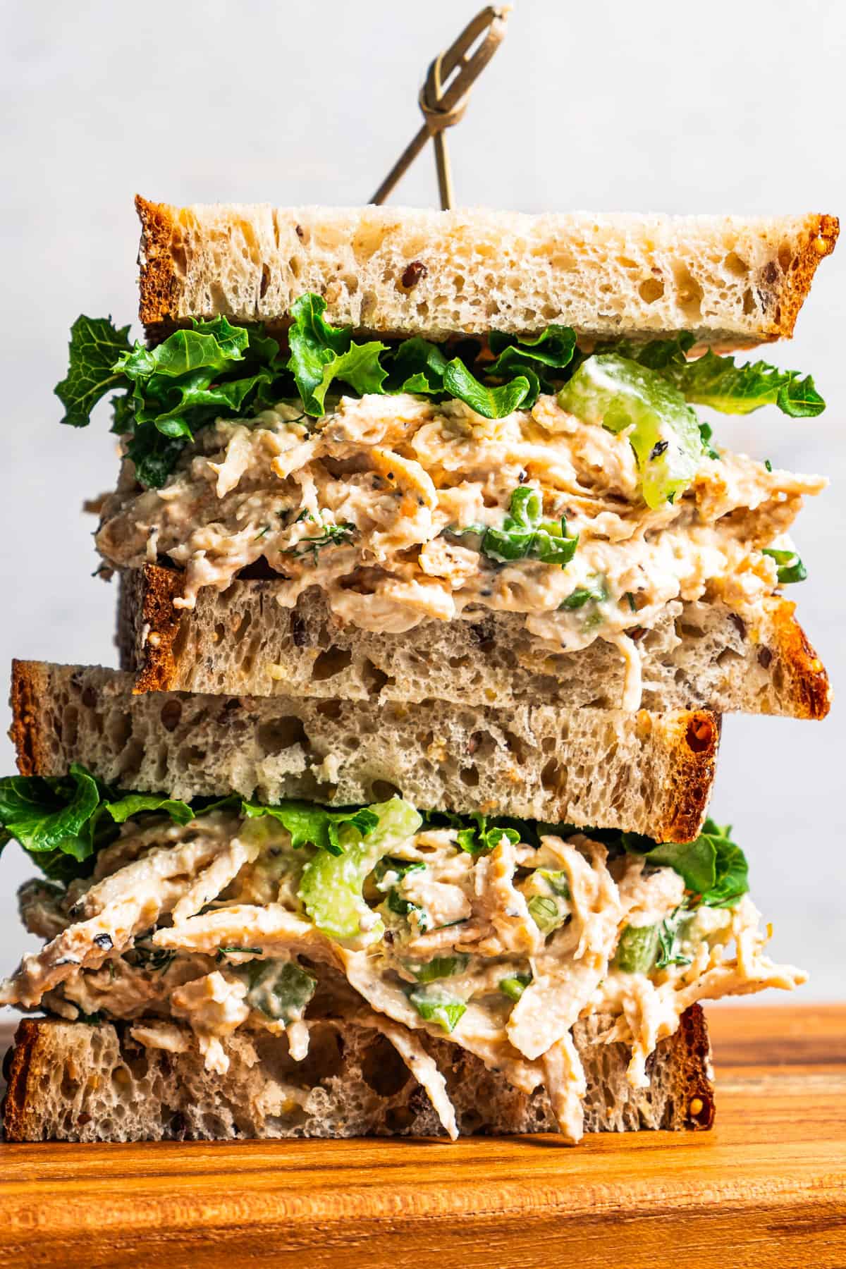 Two cottage cheese chicken salad sandwiches stacked on a wooden cutting board.