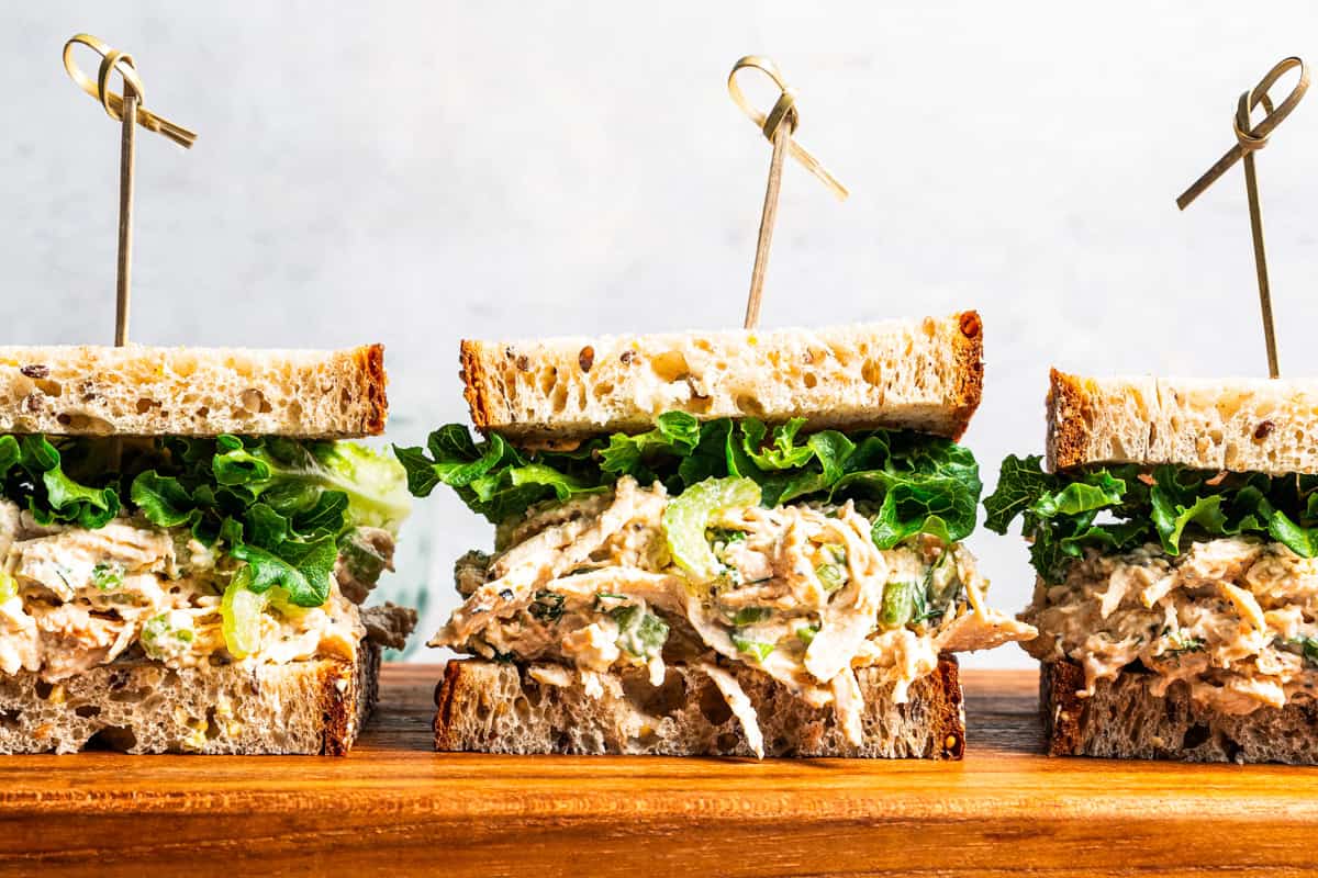 Three cottage cheese chicken salad sandwiches on a wooden cutting board.
