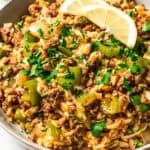 Dirty rice garnished with herbs and lemon slices in a bowl.