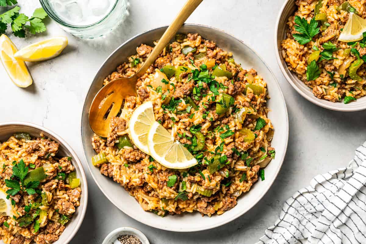 Three bowls of dirty rice garnished with herbs and lemon slices.