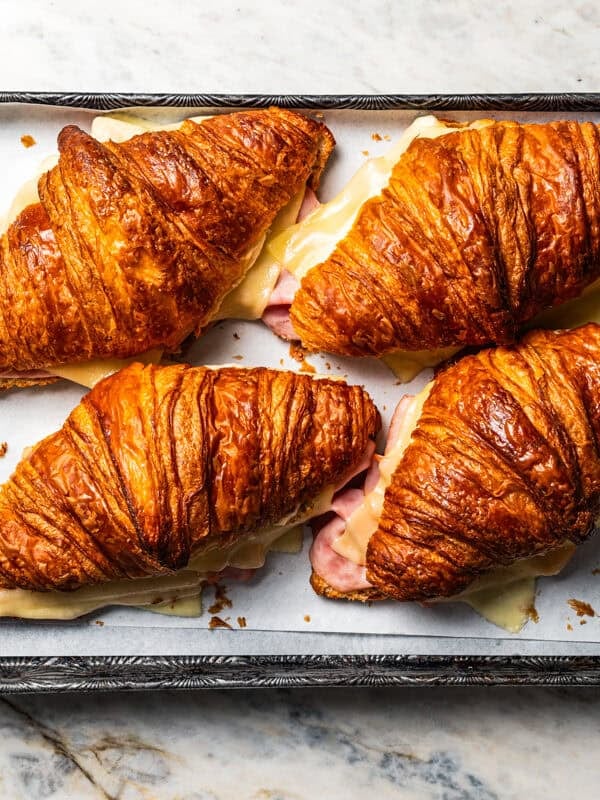 Four closed ham and cheese croissants on a baking sheet.