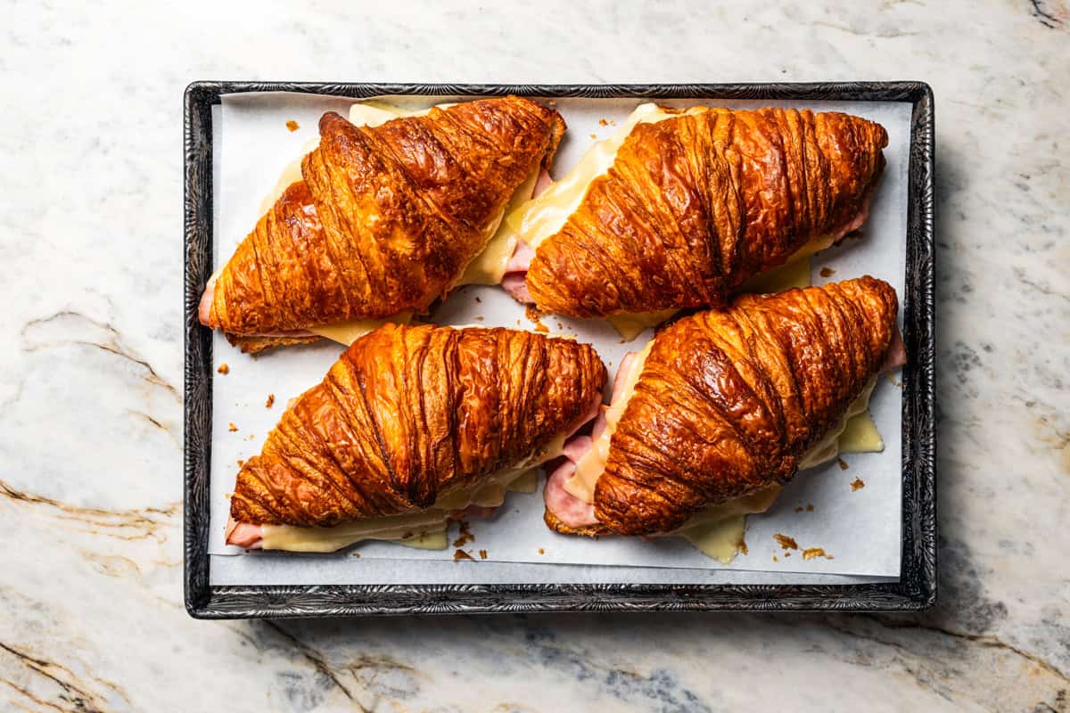 Four closed ham and cheese croissants on a baking sheet.