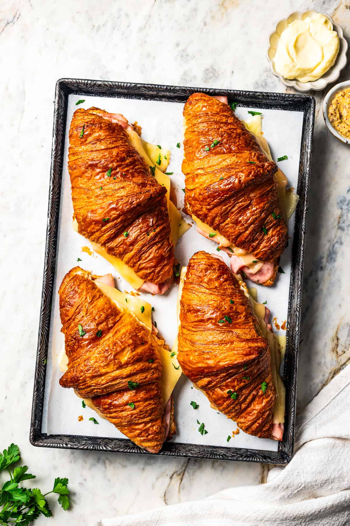 Four baked ham and cheese croissants on a baking sheet.