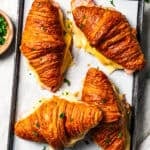 Four baked ham and cheese croissants on a baking sheet.