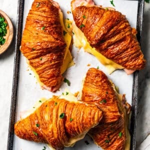 Four baked ham and cheese croissants on a baking sheet.