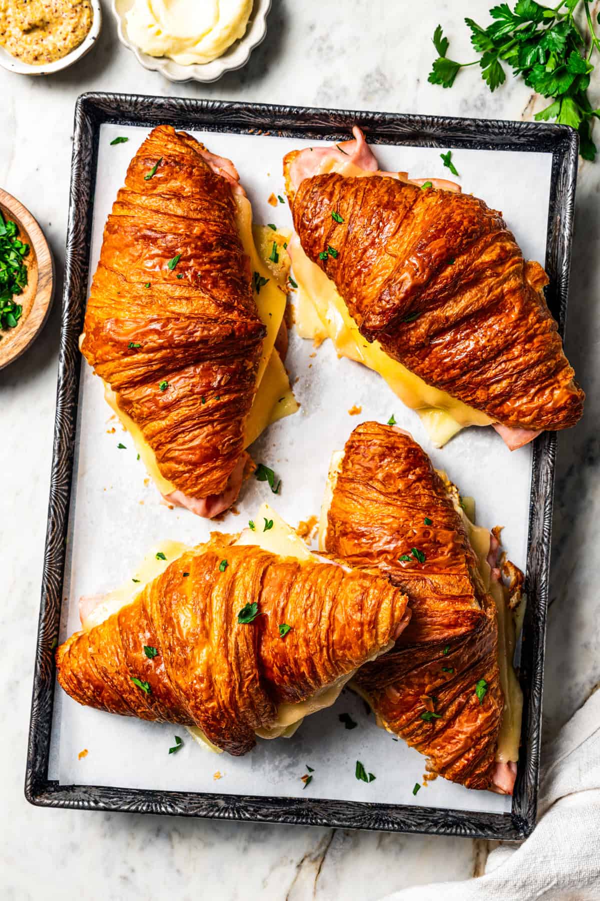Four baked ham and cheese croissants on a baking sheet.