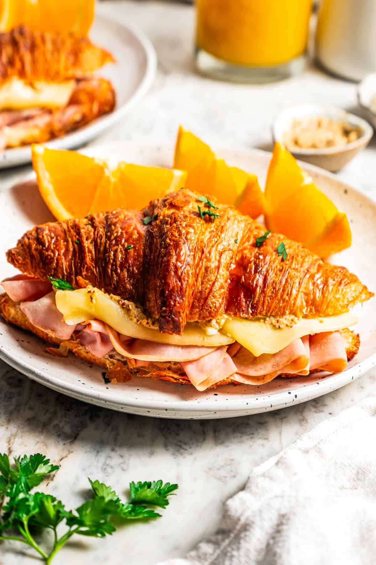 A ham and cheese croissant with orange wedges on a plate.