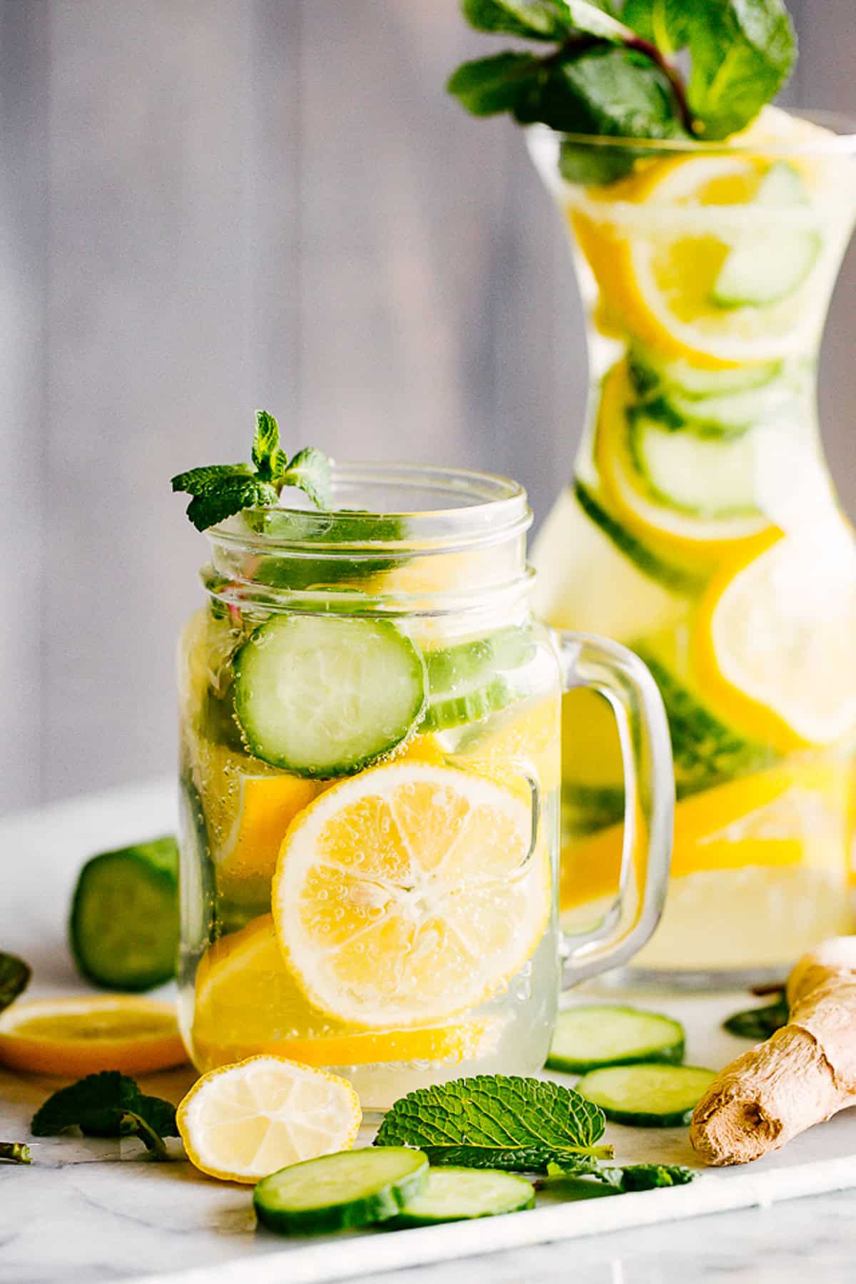 A mason jar and a carafe filled with lemon slices, cucumber slices, and water.