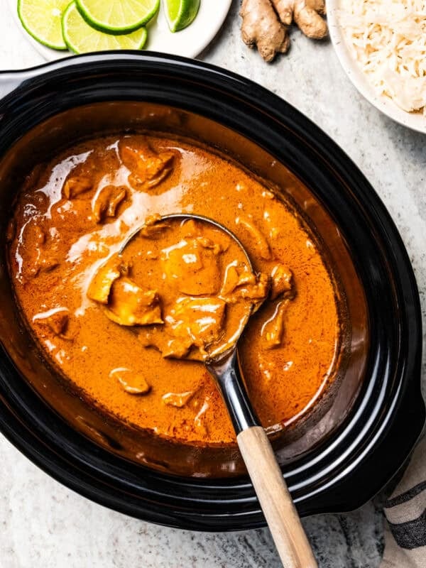 A ladle mixing through a pot of Indian butter chicken.