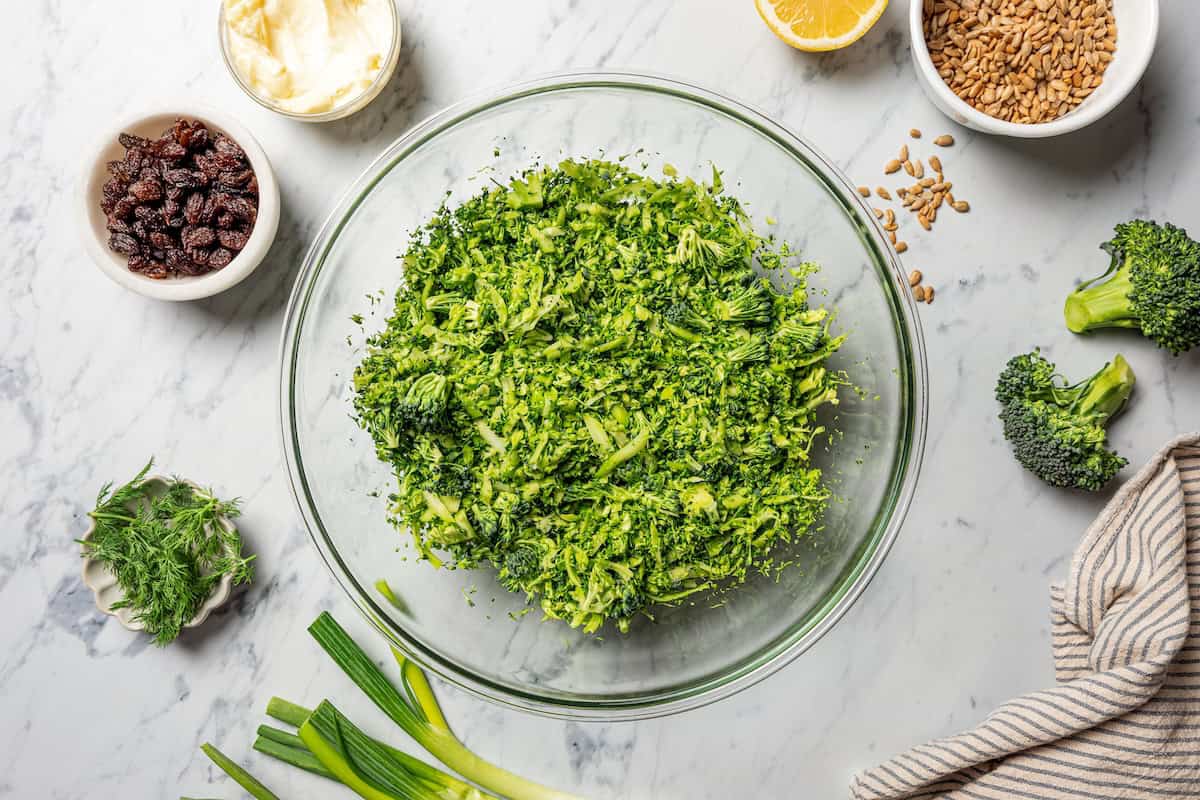 This broccoli slaw recipe is a fresh, 10-minute side dish with crunchy broccoli, sunflower seeds, and raisins in creamy buttermilk dressing. Shredded broccoli in a bowl.