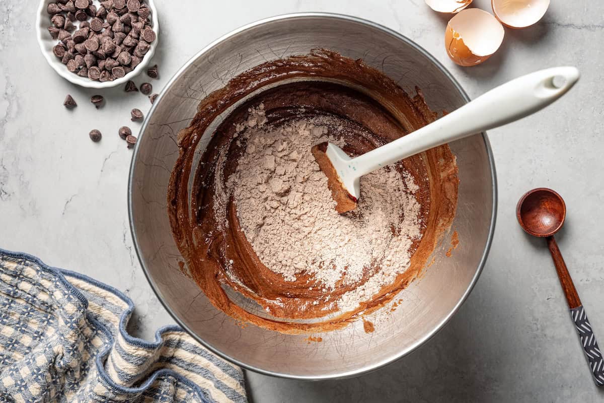 These chewy brownie cookies are the best of a fudgy brownie crossed with a soft-baked chocolate cookie! Made with real melted chocolate. Dry ingredients being folded into wet brownie cookie batter in a bowl.