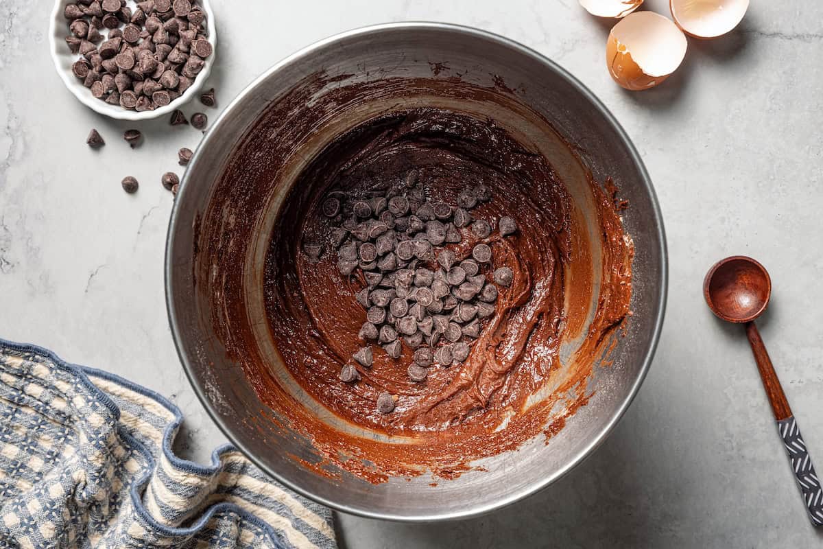 These chewy brownie cookies are the best of a fudgy brownie crossed with a soft-baked chocolate cookie! Made with real melted chocolate. Chocolate chips added to brownie cookie dough in a bowl.