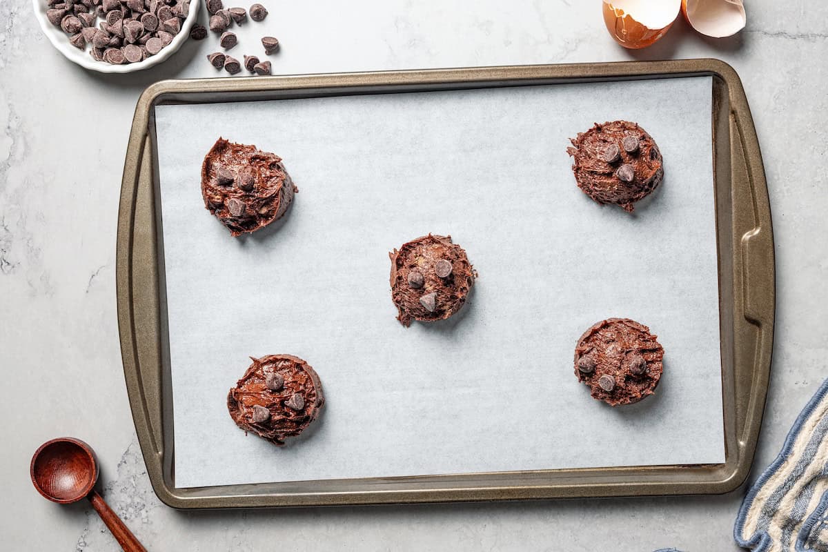 These chewy brownie cookies are the best of a fudgy brownie crossed with a soft-baked chocolate cookie! Made with real melted chocolate. Brownie cookie dough with chocolate chips portioned into balls on a baking sheet.
