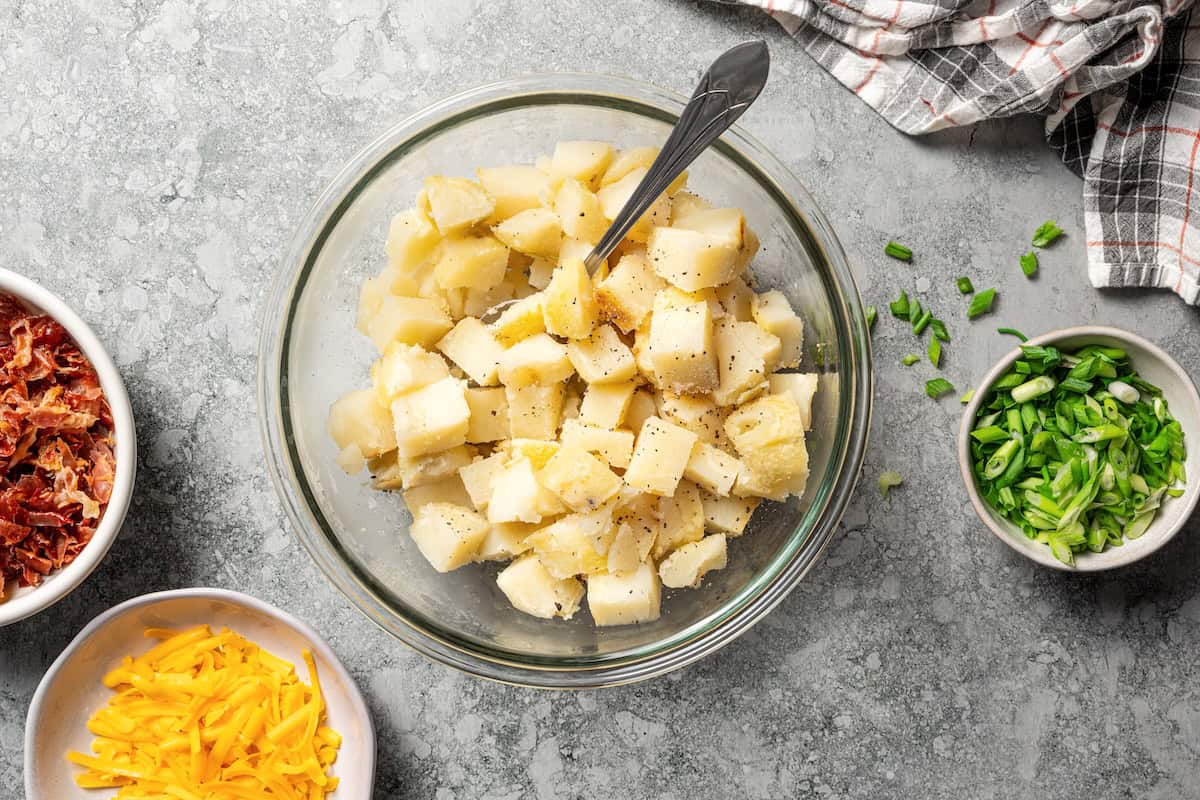 This rich and creamy loaded potato salad with bacon, spring onions, and cheddar cheese is easy to make ahead, perfect for potlucks and BBQs! Chopped baked potatoes in a bowl.