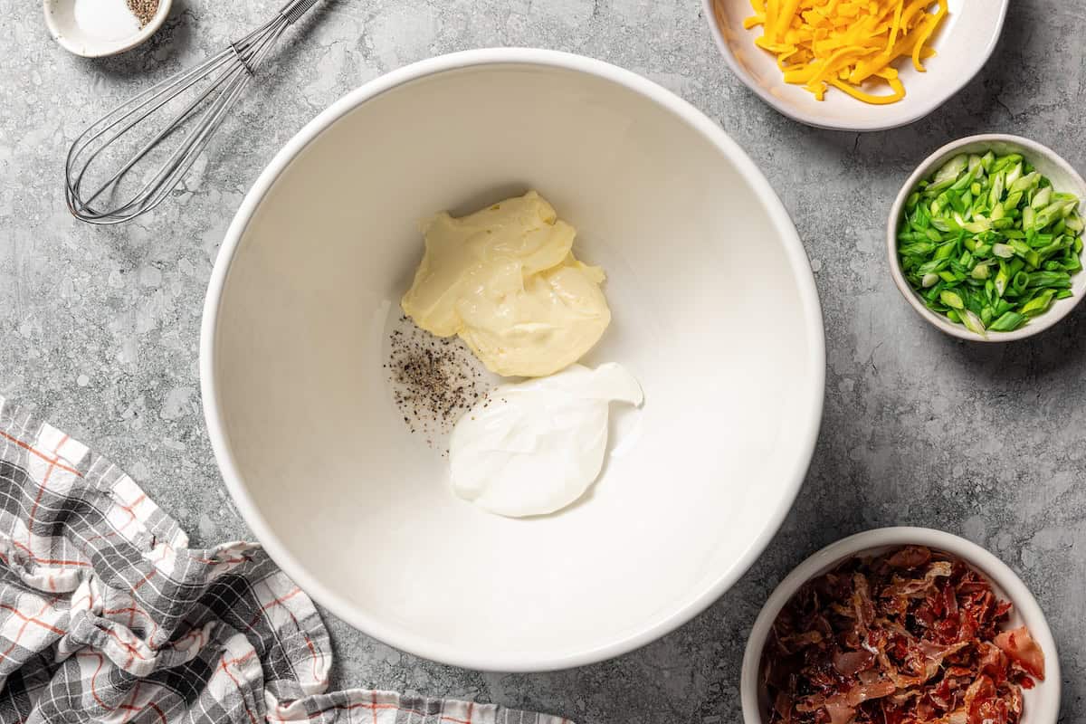 This rich and creamy loaded potato salad with bacon, spring onions, and cheddar cheese is easy to make ahead, perfect for potlucks and BBQs! Potato salad dressing ingredients combined in a bowl.