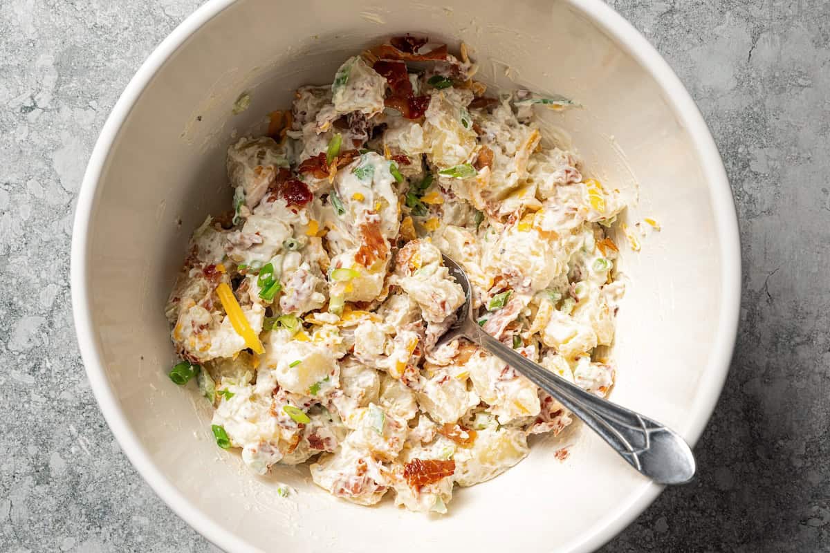 This rich and creamy loaded potato salad with bacon, spring onions, and cheddar cheese is easy to make ahead, perfect for potlucks and BBQs! Finished creamy loaded potato salad in a bowl.