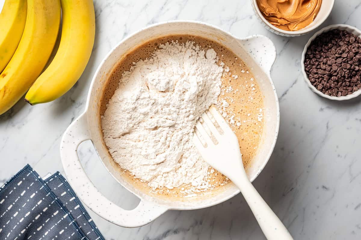 Peanut butter banana muffins are easy to make in one bowl! They’re super moist, with ripe bananas, creamy peanut butter, and chocolate chips. Dry ingredients added to wet muffin batter in a bowl.