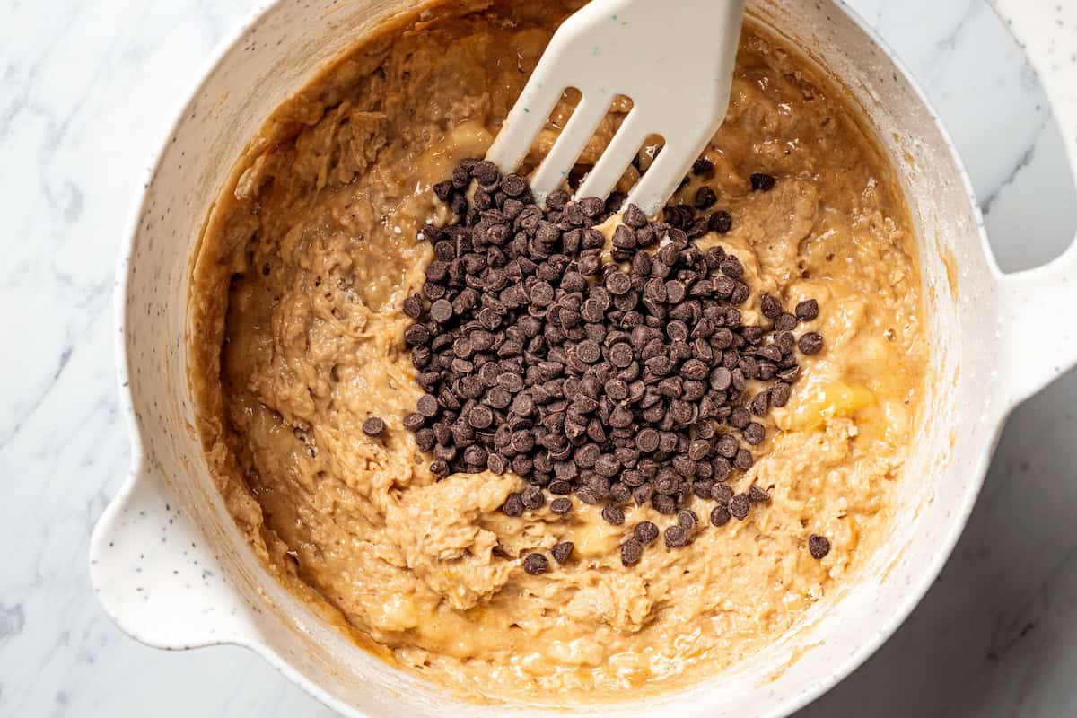 Peanut butter banana muffins are easy to make in one bowl! They’re super moist, with ripe bananas, creamy peanut butter, and chocolate chips. Chocolate chips added to peanut butter banana muffin batter in a bowl.