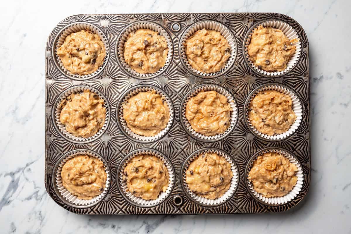Peanut butter banana muffins are easy to make in one bowl! They’re super moist, with ripe bananas, creamy peanut butter, and chocolate chips. Peanut butter banana muffin batter portioned into the lined wells of a muffin pan.