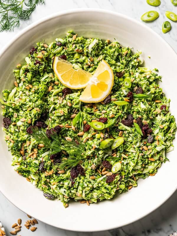 Broccoli slaw served in a salad bowl and garnished with lemon wedges and fresh green herbs.